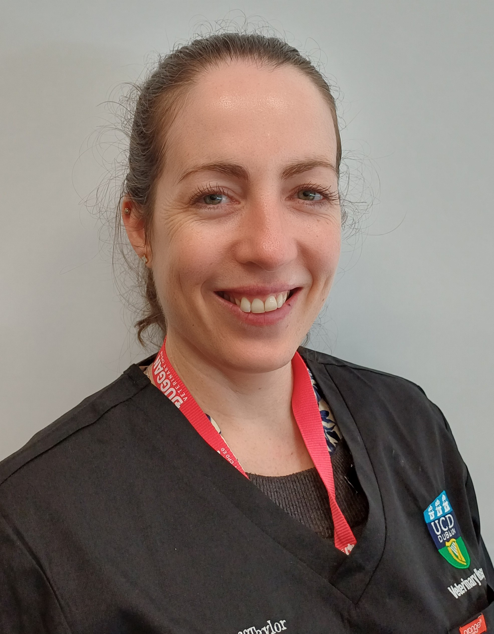 Andrea Kilduff-Taylor smiles while wearing navy scrubs and a pink lanyard